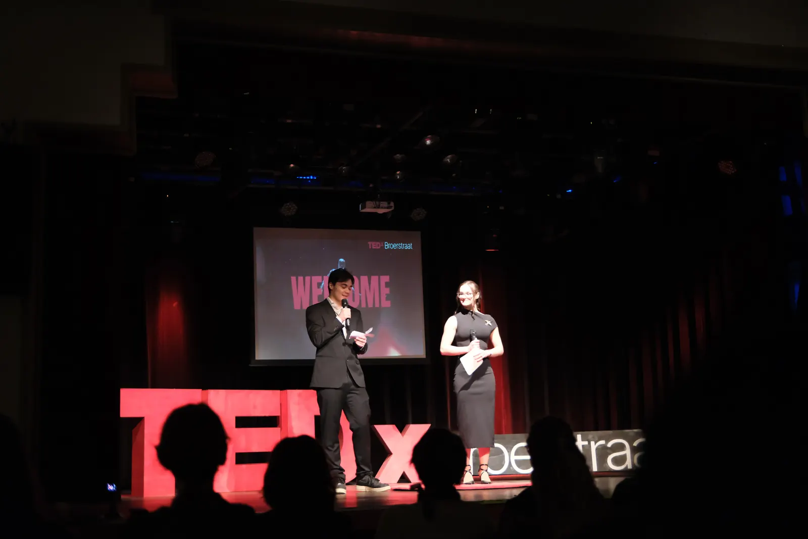 Two hosts on stage at a TEDx event.